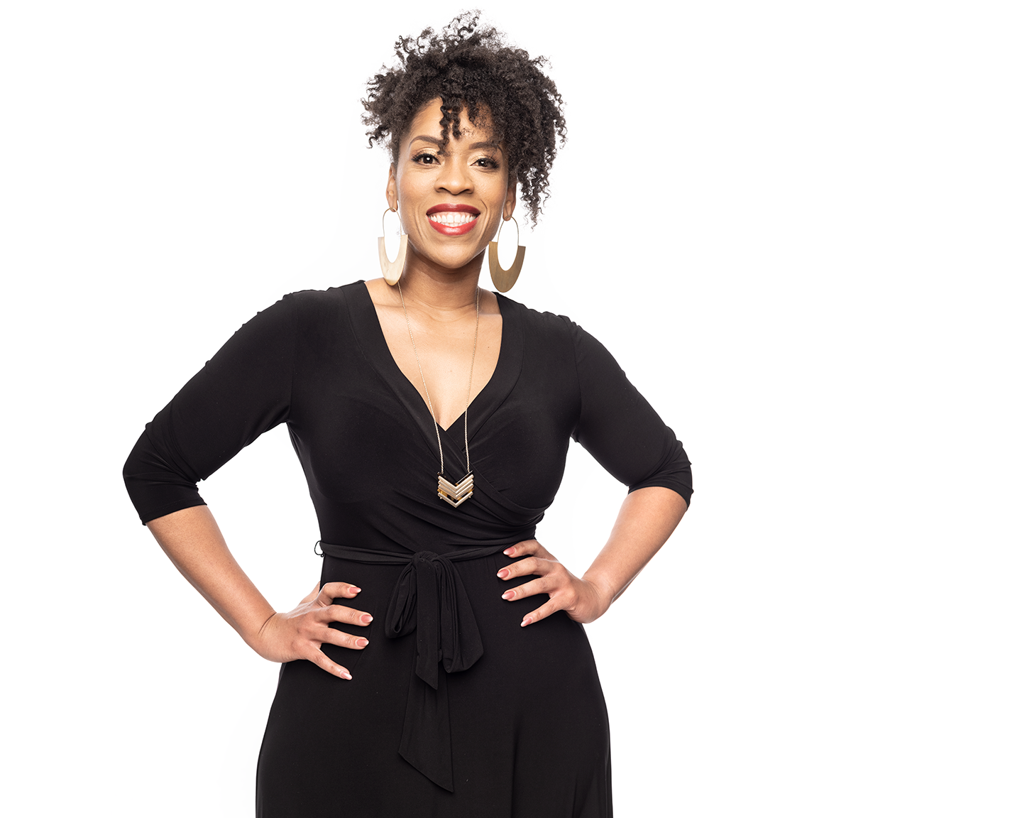 Light brown African-American woman with curly black hair, in a black wrap dress and gold jewelry in front of a white background.